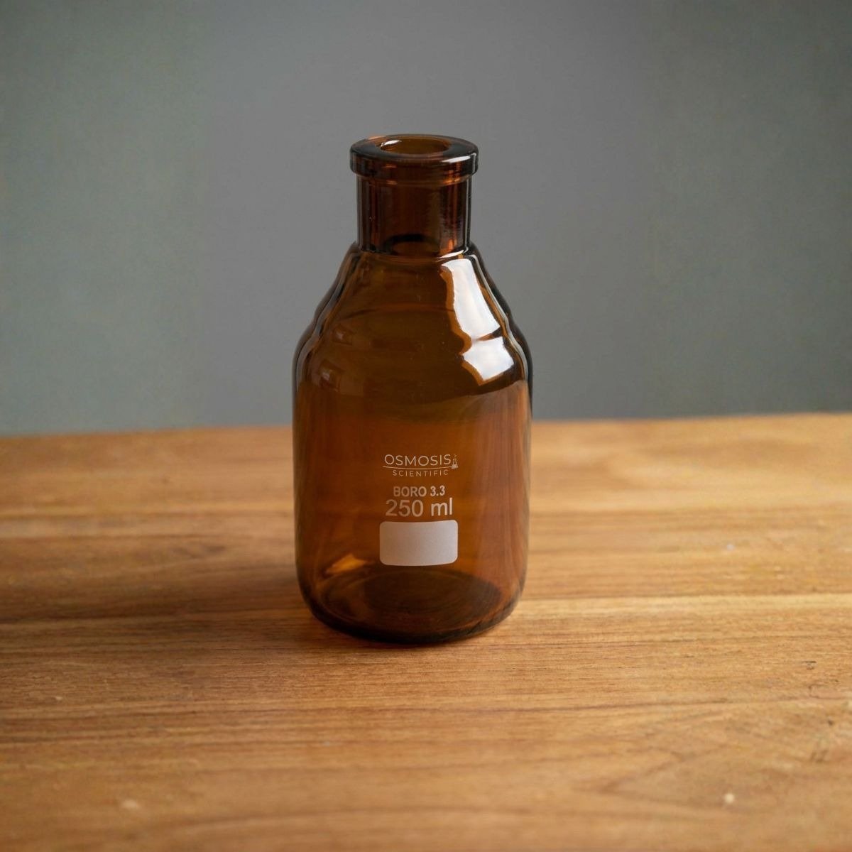A 250ml amber borosilicate glass reagent bottle featuring a reinforced tooled neck and a white marking square, set on a wooden surface.