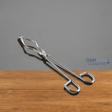 A pair of professional-grade stainless steel crucible tongs with serrated tips and finger loops, resting on a polished wooden surface.