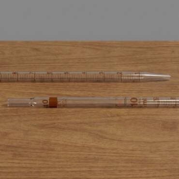 Clear borosilicate glass Class A serological graduated pipettes with brown enamel markings and a 10ml capacity, shown in detail on a wooden surface.