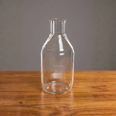 A 500ml clear borosilicate glass reagent bottle with a reinforced tooled neck and a white marking square, displayed on a wooden surface.